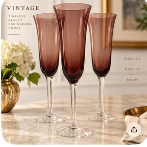 May include: Three tall champagne flutes with deep purple-tinted bowls and clear glass stems and bases. The text VINTAGE TIMELESS BEAUTY FOR MODERN HOMES is visible on the left, and COLLECT DISPLAY ENJOY is visible on the right side of the image.