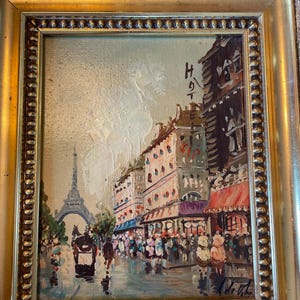 May include: An oil painting in a decorative gold frame depicting a Parisian street scene with the Eiffel Tower in the background. The artwork features a horse-drawn carriage, pedestrians, and buildings with the text HOTEL visible on a facade.
