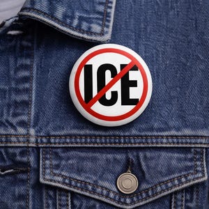 May include: A white button with a red border and a red slash through the word "ICE" in black letters. The button is pinned to a blue denim jacket.