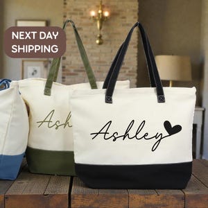 May include: Cream-colored tote bags with black and olive green accents. One bag has the name "Ashley" with a heart, and another has the name "Ash" in a script font. The bags have sturdy handles and a color-blocked design.