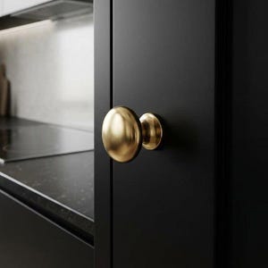 K&ouml;nnte beinhalten: Nahaufnahme eines goldfarbenen Schrankknaufs an einer schwarzen Schrankt&uuml;r. Der Knauf hat eine abgerundete, ovale Form. Die K&uuml;chenumgebung umfasst eine Arbeitsplatte und eine R&uuml;ckwand.