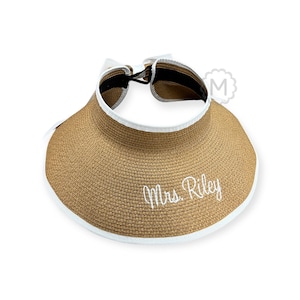 May include: A brown straw sun hat with a white trim and a white embroidered inscription that reads "Mrs. Riley".
