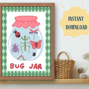 Può includere: Un ricamo a punto croce incorniciato raffigurante un barattolo pieno di insetti colorati. Il barattolo ha un coperchio rosa e contiene una coccinella, una mantide religiosa, una farfalla e altri insetti. La scritta "BUG JAR" è ricamata sotto.