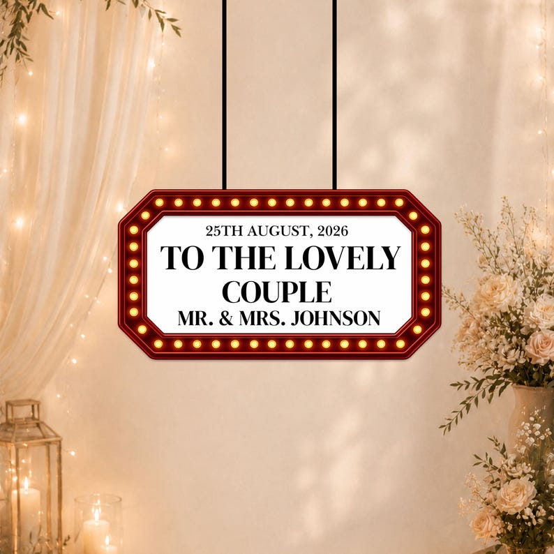 May include: A rectangular sign with a red border and small lights, hanging from black cords. The sign reads "25th August, 2026" and "TO THE LOVELY COUPLE MR. & MRS. JOHNSON" in a classic font. The background is a soft, warm color.