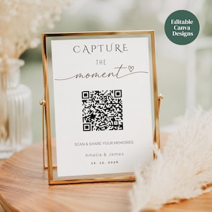 Op de afbeelding: Een verticaal rechthoekig bord in een gouden metalen frame met de tekst CAPTURE THE moment en een hartpictogram, een centrale QR-code, de tekst SCAN & SHARE YOUR MEMORIES, en de namen Amelia & James met de datum 12. 12. 2026 eronder gedrukt.
