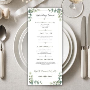 May include: A vertical rectangular wedding menu card featuring a white background with green watercolor eucalyptus leaf illustrations at the top and bottom corners. The text reads Wedding Feast, Refreshing Starters, Tasty Bites, Chef's Specials, Sweet Endings, and With Love A & B.