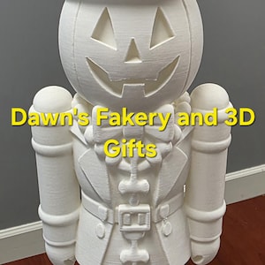 Puede incluir: Figura de cascanueces blanca impresa en 3D con temática de Halloween. La figura tiene una cabeza de calabaza con una cara tallada, un sombrero de copa con un detalle de hueso y un uniforme de estilo militar. La base es redonda.