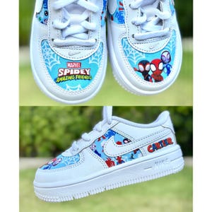 K&ouml;nnte beinhalten: Wei&szlig;e Turnschuhe mit blauen und roten Spidey-Grafiken. Die Schuhe zeigen den Text "MARVEL SPIDEY AMAZING FRIENDS" und den Namen "CARTER". Der Nike-Swoosh ist sichtbar.