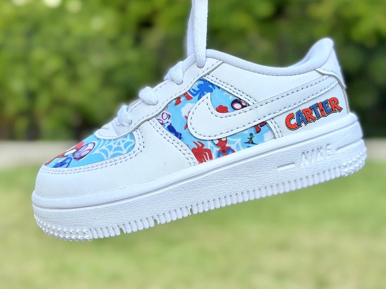 K&ouml;nnte beinhalten: Wei&szlig;er Nike Air Force 1 Sneaker mit individuellem Spider-Man-Design. Der Schuh hat ein blaues und rotes Muster mit Spider-Man-Grafiken. Der Name "CARTIER" ist rot und blau auf der Seite aufgedruckt.