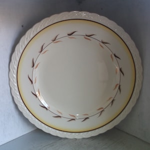May include: A white ceramic dinner plate with a yellow and brown rim and a brown leaf design.