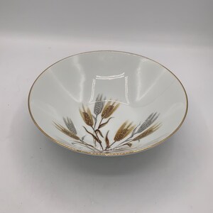 Może przedstawiać: Biała ceramiczna miska ze złotym obramowaniem i wzorem kłosów pszenicy w odcieniach brązu i szarości. Miska ma prosty, elegancki design, odpowiedni do serwowania lub ekspozycji.