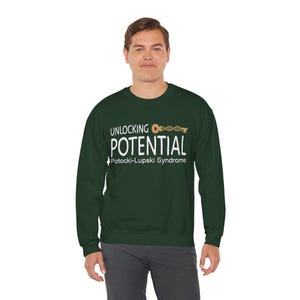 May include: A dark green sweatshirt with the words "UNLOCKING POTENTIAL" in white, with a DNA strand and key graphic. Below the text is "Potocki-Lupski Syndrome" in white. The sweatshirt is a crew neck style.