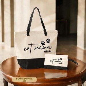 A white tote bag with black trim and paw prints, and a smaller white bag with the same paw print design, both labeled "cat mama Olivia" on a wooden table.