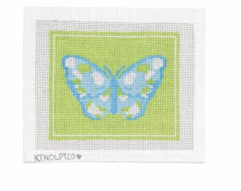 May include: A needlepoint canvas featuring a butterfly design. The butterfly is light blue with white accents, set against a green background within a white border. The text "KINDLPTCO" is visible at the bottom.