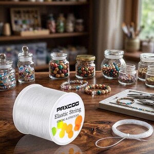 May include: A spool of clear PAXCOO Elastic String with a white label featuring the text 'PAXCOO Elastic String STRONG & STRETCHY' and colorful circular graphics, accompanied by a coiled length of the same string and various glass jars of beads.