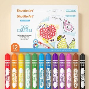Peut inclure: Un ensemble de 12 marqueurs à points lavables Shuttle Art dans une boîte blanche avec des illustrations colorées d'une pomme et de poires. Les marqueurs sont alignés, incluant les couleurs rouge, orange, jaune, vert émeraude, vert, bleu aqua, bleu océan, violet, pourpre, fuchsia, terre d'ombre brûlée et noir.