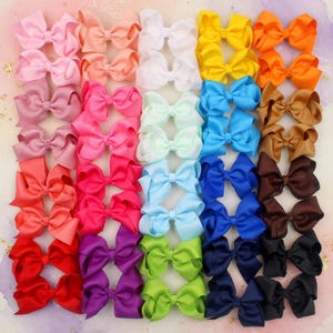 May include: A selection of colourful hair bows in shades of pink, white, yellow, orange, blue, brown, green, purple, and black. The bows are arranged in rows, displaying their vibrant colours and symmetrical designs. These accessories are ideal for adding a touch of flair to any hairstyle.