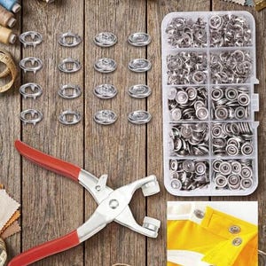 May include: A metal snap fastener kit featuring a pair of pliers with red handles, a clear plastic storage container filled with silver-colored metal snap buttons, and a small inset image showing the snaps installed on a yellow fabric garment.