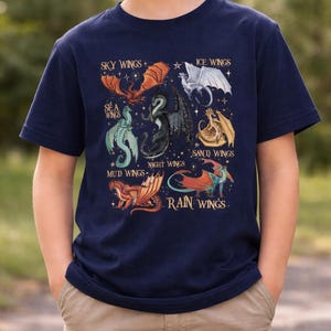 May include: Navy blue short-sleeve t-shirt featuring a colorful dragon graphic. The design includes various dragon types labeled "Sky Wings," "Ice Wings," "Sea Wings," "Sand Wings," "Night Wings," "Mud Wings," and "Rain Wings."