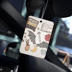 May include: Rectangular air freshener with a collection of whimsical illustrations. The design includes a miniature cabinet with flowers, a sword, bat wings, a rose, a crescent moon, and the text "hello flyre darling chapter 53".