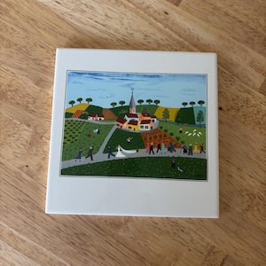 May include: A square ceramic tile featuring a colorful folk art scene of a wedding procession in a rural village. The artwork depicts a church, fields, and figures walking along a path. The tile is white with a glossy finish.