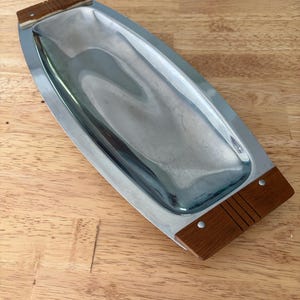May include: A rectangular serving tray with a polished silver interior and wooden handles. The wooden handles are a warm brown color and are attached to the tray with small silver rivets. The tray is on a wooden surface.