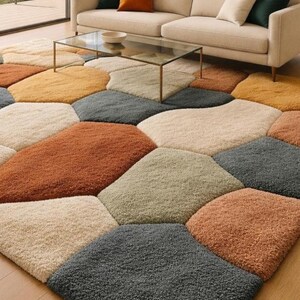 May include: A multi-colored area rug with a geometric pattern. The rug features various earth-tone colors, including beige, orange, yellow, and gray. The rug is placed in a living room setting, with a sofa and coffee table visible in the background.