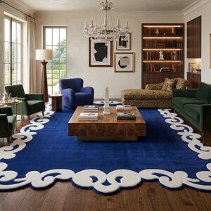 May include: A luxurious living room featuring a large, deep blue rug with a white, ornate border. The room includes green and blue armchairs, a dark green sofa, a wooden coffee table, and a crystal chandelier. Artwork and a patterned chaise lounge add to the elegant decor.