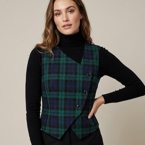 以下が含まれることがあります： 3つの黒いボタンが付いた、緑とネイビーのチェック柄ベスト。黒の長袖トップスの上に着用し、黒いパンツと合わせています。ベストのチェック柄はクラシックなデザインです。