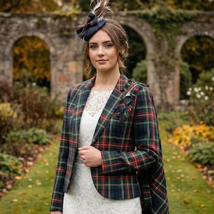 Könnte beinhalten: Eine Frau trägt einen Blazer mit rot-, grün- und marineblauen Karomuster. Dazu ein weißes Spitzenkleid und ein passender Hut. Im Hintergrund ein Steinbogen und herbstliches Laub.