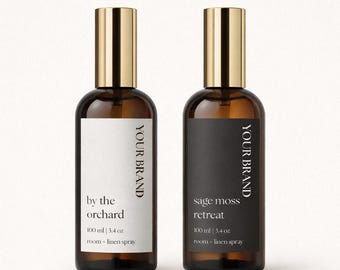 May include: Two amber glass spray bottles with gold-colored caps. One label reads "by the orchard" and the other reads "sage moss retreat". Each bottle contains 100 ml | 3.4 oz of room-linen spray. The brand name is printed vertically.