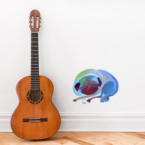 May include: Acoustic guitar with a natural wood finish, next to a wall with a colourful illustration of a curled-up pug dog. The dog illustration features shades of blue, green, and red.