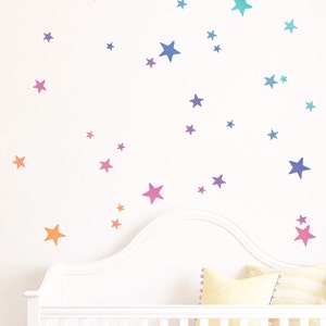 May include: A white wall with a cot in front of it. The wall is decorated with a variety of colourful star stickers in shades of pink, orange, yellow, blue, and purple.