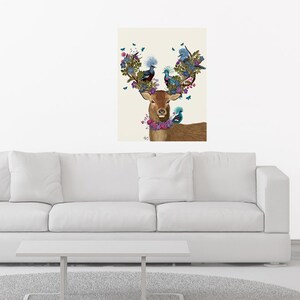 Puede incluir: Una impresión artística enmarcada que presenta un ciervo marrón con astas florales y un collar floral. Las astas están adornadas con pájaros y flores azules y verdes. Mariposas están dispersas alrededor del ciervo. La obra de arte se exhibe sobre un sofá blanco y una mesa de centro blanca.