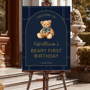 May include: A navy blue sign on an easel with a teddy bear illustration and the text "Welcome to William's Beary First Birthday 20.08.2026". The sign has a plaid pattern and gold accents.