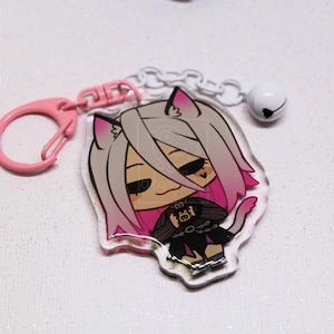 May include: An acrylic keychain featuring a cartoon character with light gray and pink hair, cat ears, and a black outfit. The charm is attached to a pink plastic clasp and a white chain with a small white bell. The logo a-happy-Jake is visible.