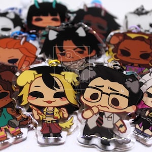 May include: A collection of clear acrylic charms featuring various illustrated chibi-style characters with diverse hair colors, outfits, and expressions. Each charm includes a small metal loop for attachment and a small logo in the corner.
