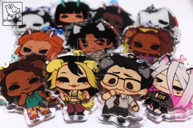 May include: A collection of clear acrylic charms featuring various illustrated chibi-style characters with diverse hair colors, outfits, and expressions. Each charm includes a small metal loop for attachment and a small logo in the corner.