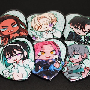Op de afbeelding: Zes hartvormige pins met chibi-stijl anime-personages met diverse haarkleuren en outfits, tegen een lichtgroene rasterachtergrond. Elke pin toont een uniek personage, waaronder een met een gitaar, allemaal met zwarte randen.