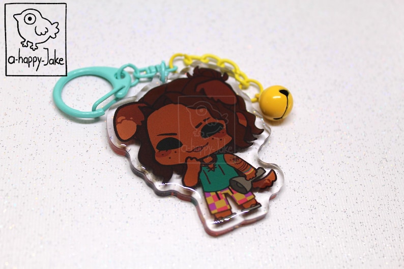 May include: An acrylic keychain featuring a cartoon character with brown fur, wearing a green shirt and checkered pants, holding a gray plunger. The charm is attached to a light blue plastic clasp and a yellow chain with a small yellow bell.