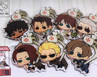 May include: A collection of seven clear acrylic charms featuring chibi-style characters from Resident Evil, each being lifted by a claw machine mechanism with an Umbrella Corporation logo. The charms depict various characters with distinct hair colors.