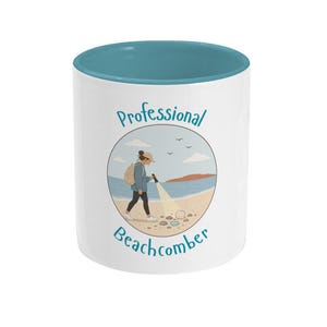 May include: White ceramic mug with a teal interior and a beachcombing illustration. The illustration shows a person searching the beach with a flashlight, with the words "Professional Beachcomber" in a circular design.