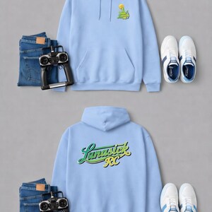 May include: Two light blue hoodies with the text "Lunastick RC" and a graphic on the front. The image also includes blue jeans, a remote control, and white sneakers with blue accents. The hoodies have a front pocket and a hood.