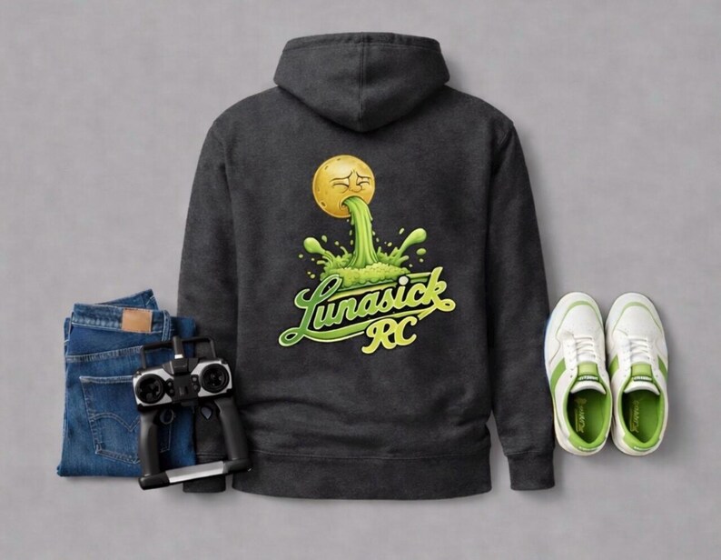 Peut inclure: Sweat &agrave; capuche gris fonc&eacute; avec un motif d'une balle jaune vomissant du liquide vert, avec le texte "Lunasick RC". L'image comprend &eacute;galement un jean bleu, une t&eacute;l&eacute;commande et des baskets blanches avec des accents verts.