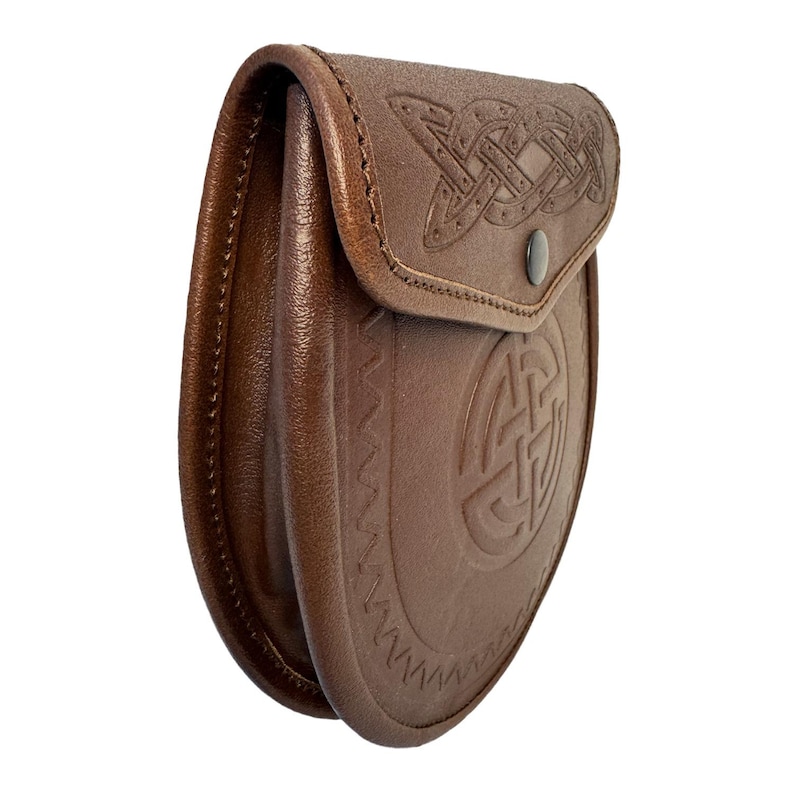 May include: A brown leather sporran with Celtic knotwork embossed on the flap and body. The sporran has a curved shape and a snap closure. The leather is a rich, medium brown color, and the stitching is visible along the edges.