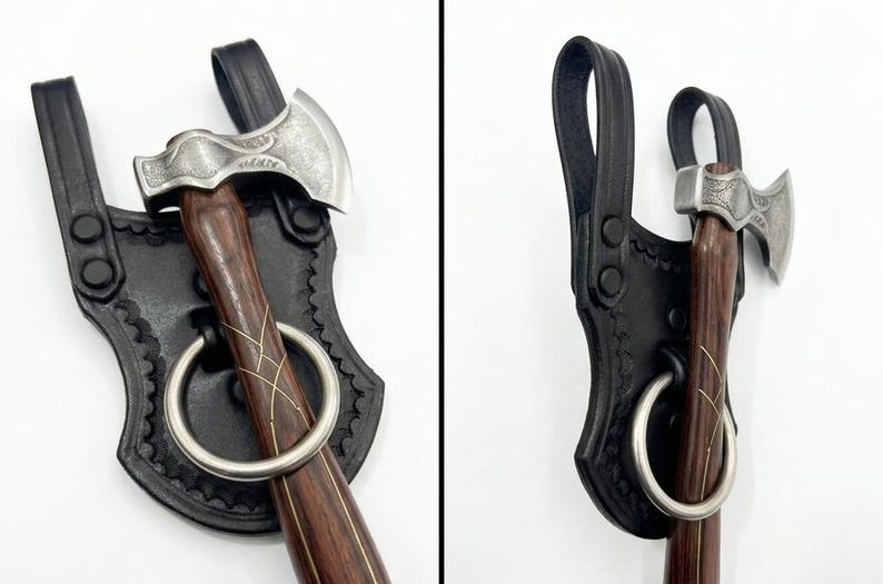 May include: A small, silver axe with a dark wooden handle and a decorative design. The axe is secured in a black leather sheath with a large metal ring. The sheath has a decorative edge and a loop for carrying.