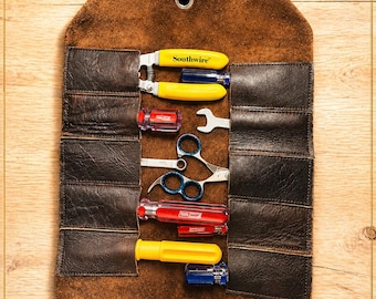 May include: A brown leather tool roll with various tools, including screwdrivers, a wrench, and scissors. The tools are arranged in pockets within the roll. The text "CRAFTED FOR WORK. BUILT TO LAST." is at the bottom.