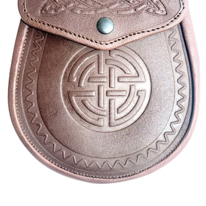 May include: A brown leather sporran with Celtic knotwork and a flap closure. The sporran features embossed designs and a decorative border. A metal button secures the flap.