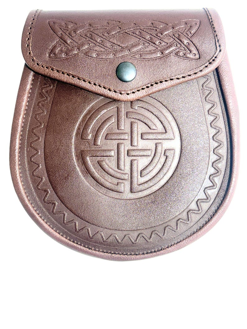 May include: A brown leather sporran with Celtic knotwork and a flap closure. The sporran features embossed designs and a decorative border. A metal button secures the flap.