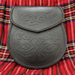 Peut inclure: Un sporran en cuir noir avec un motif de n&oelig;uds celtiques en relief. Le sporran est dot&eacute; d'une fermeture &agrave; rabat et est pr&eacute;sent&eacute; sur un fond &agrave; carreaux rouges et noirs. Accessoire &eacute;cossais traditionnel.